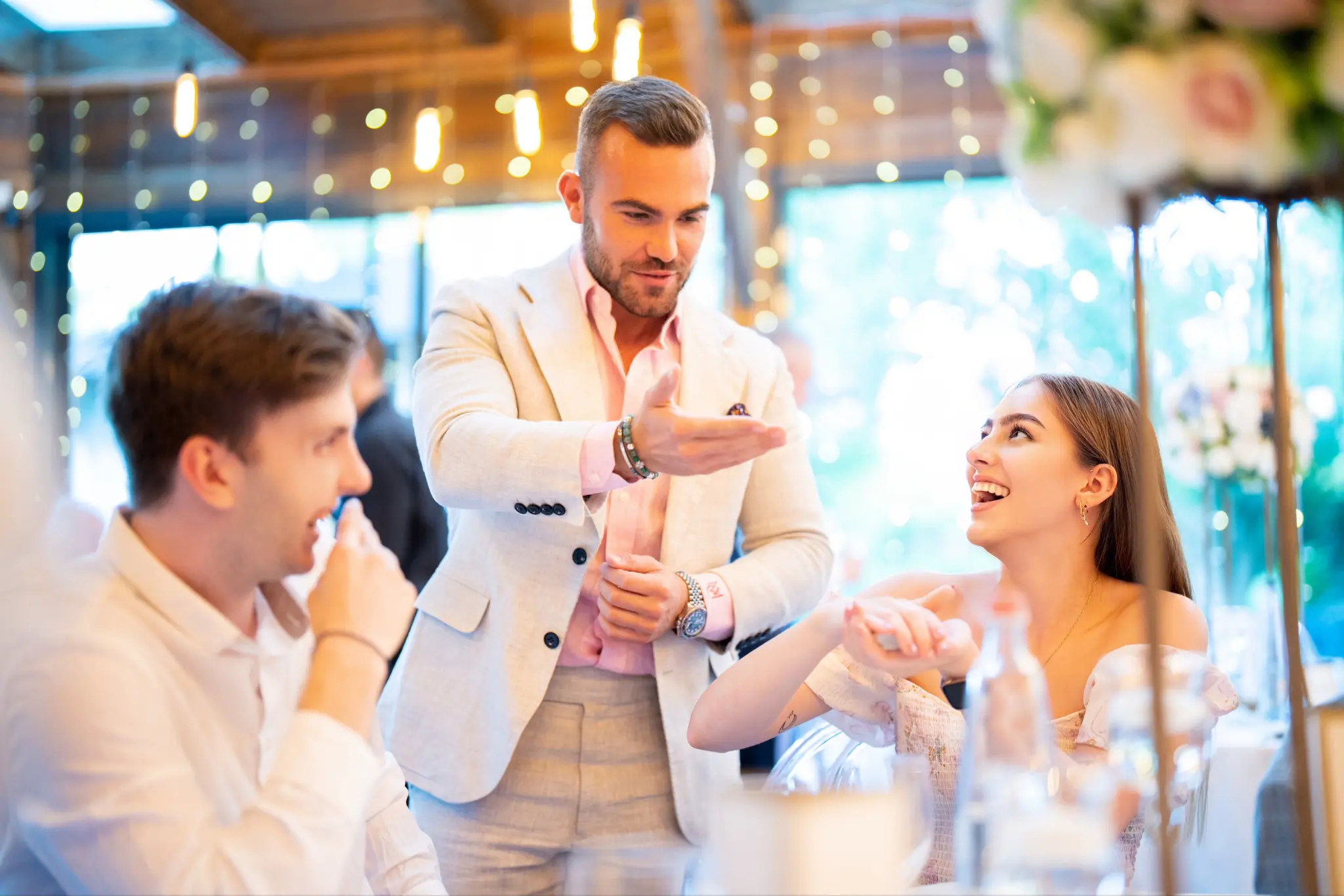 A couple reacting with joy and amazement during a close-up magic performance at their wedding reception with fairy lights in the background