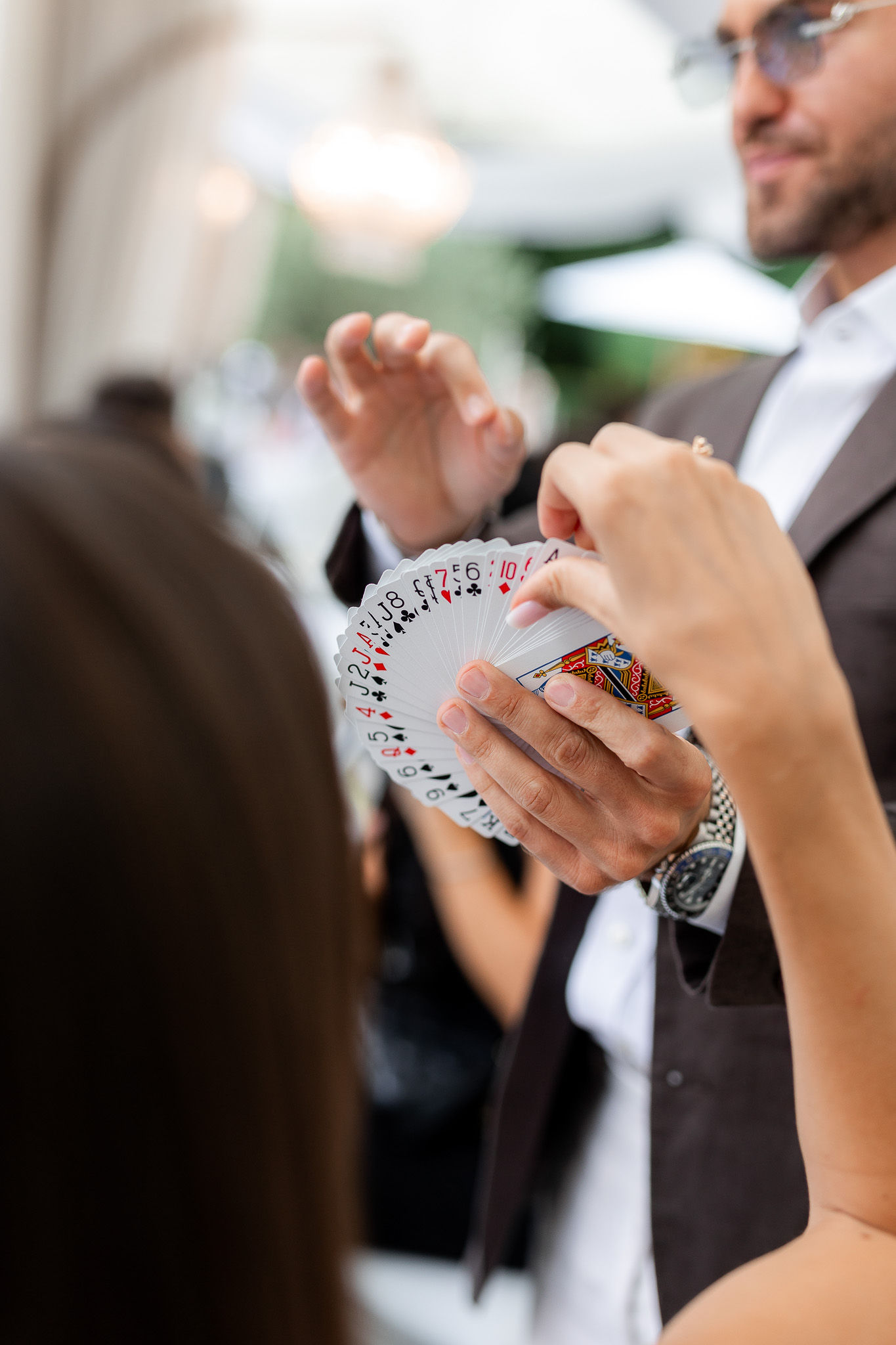 Close-up of Matteo Cammisa's hands holding a fan of playing cards as a guest reaches to select one