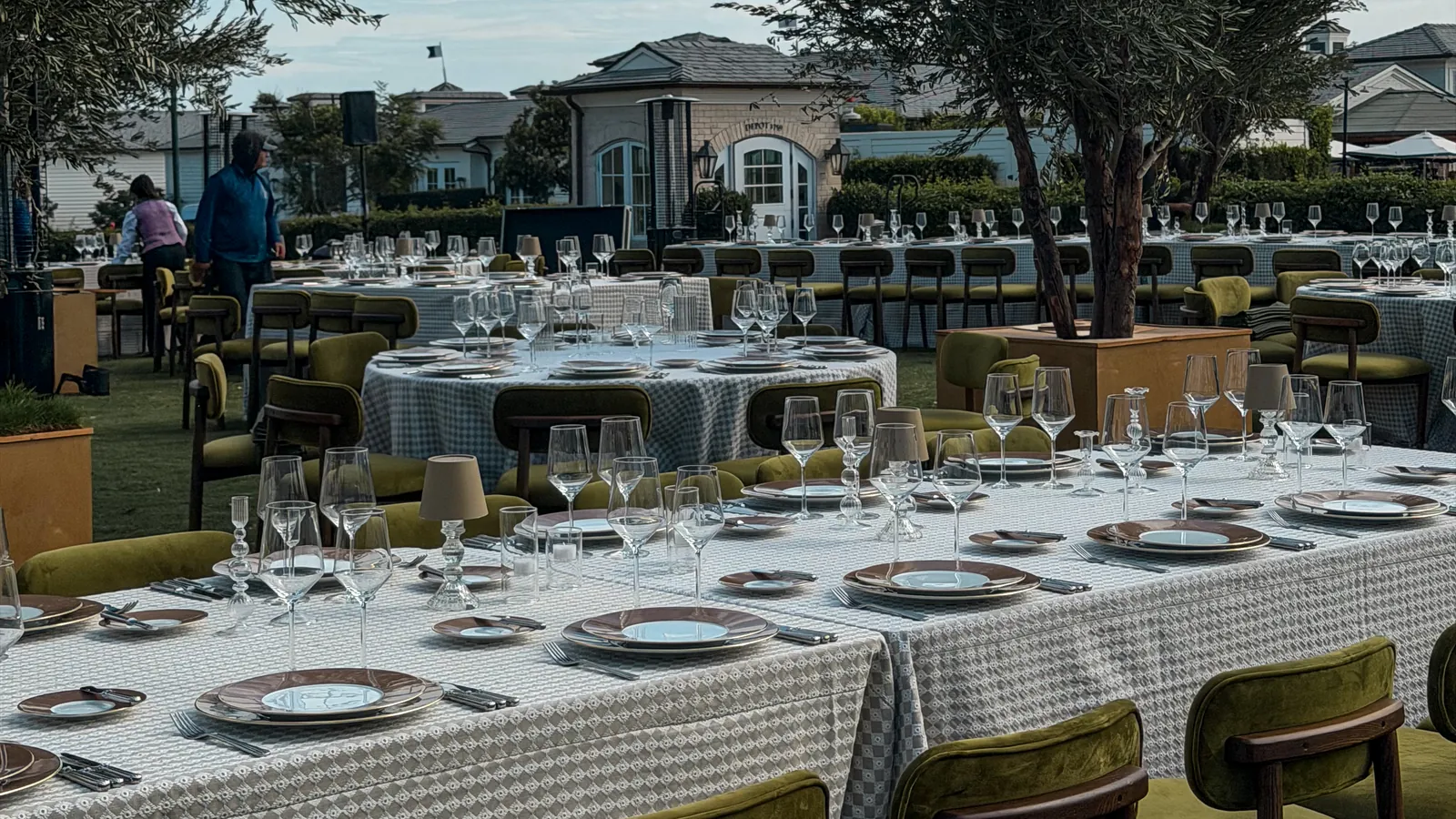 A long table laid for a wedding dinner on the lawn at Rosewood Miramar Beach, Montecito, olive trees and the clubhouse behind