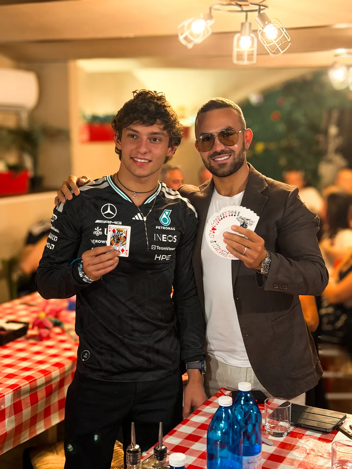 Kimi Antonelli in Mercedes-AMG Petronas race kit holding a signed King of Diamonds next to magician Matteo Cammisa with a fanned deck of cards