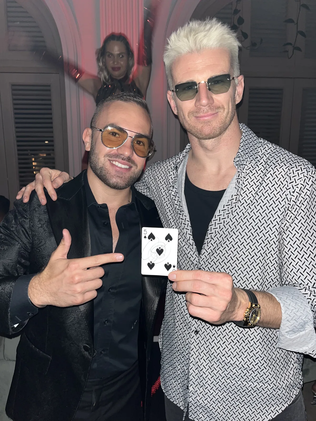 Nico Hülkenberg holding a signed five of spades while magician Matteo Cammisa points at the card