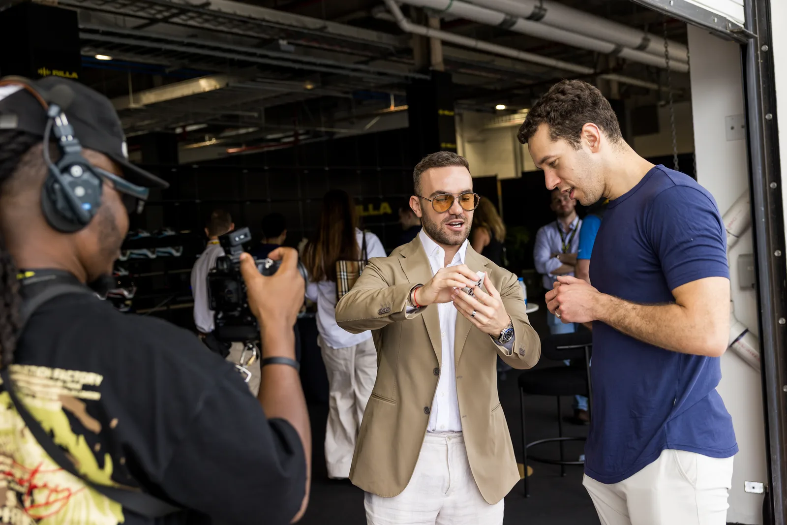 A videographer filming Matteo Cammisa performing close-up magic in a garage at the Miami International Autodrome