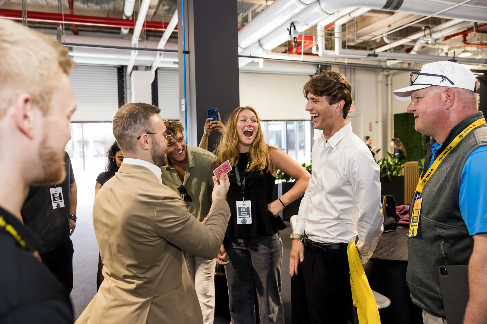 A guest laughing in astonishment mid-trick as Matteo Cammisa performs in a Miami race-week hospitality space