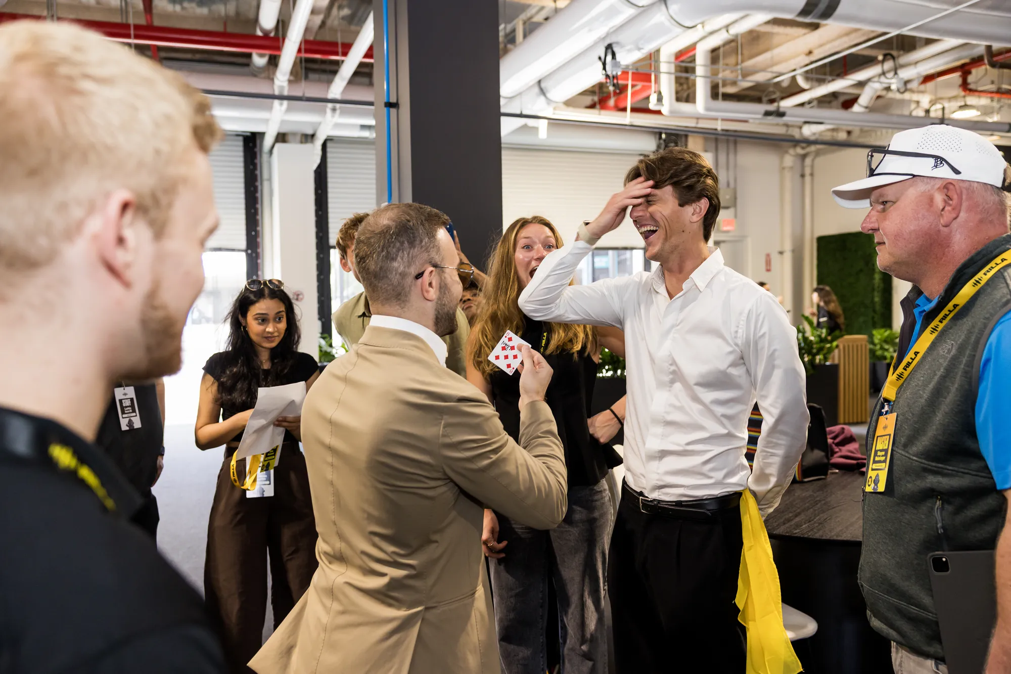 Guests reacting with laughter and astonishment as Matteo Cammisa reveals a signed card at a Miami race-week hospitality event