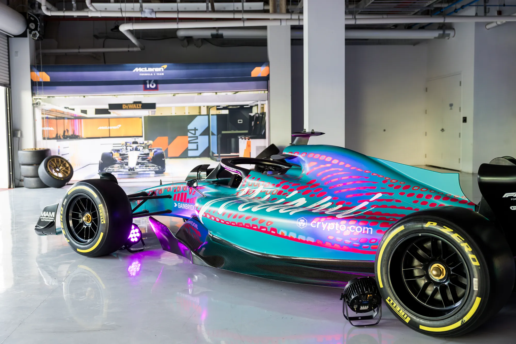 A Miami Grand Prix show car in a garage with a McLaren Formula 1 team pit backdrop