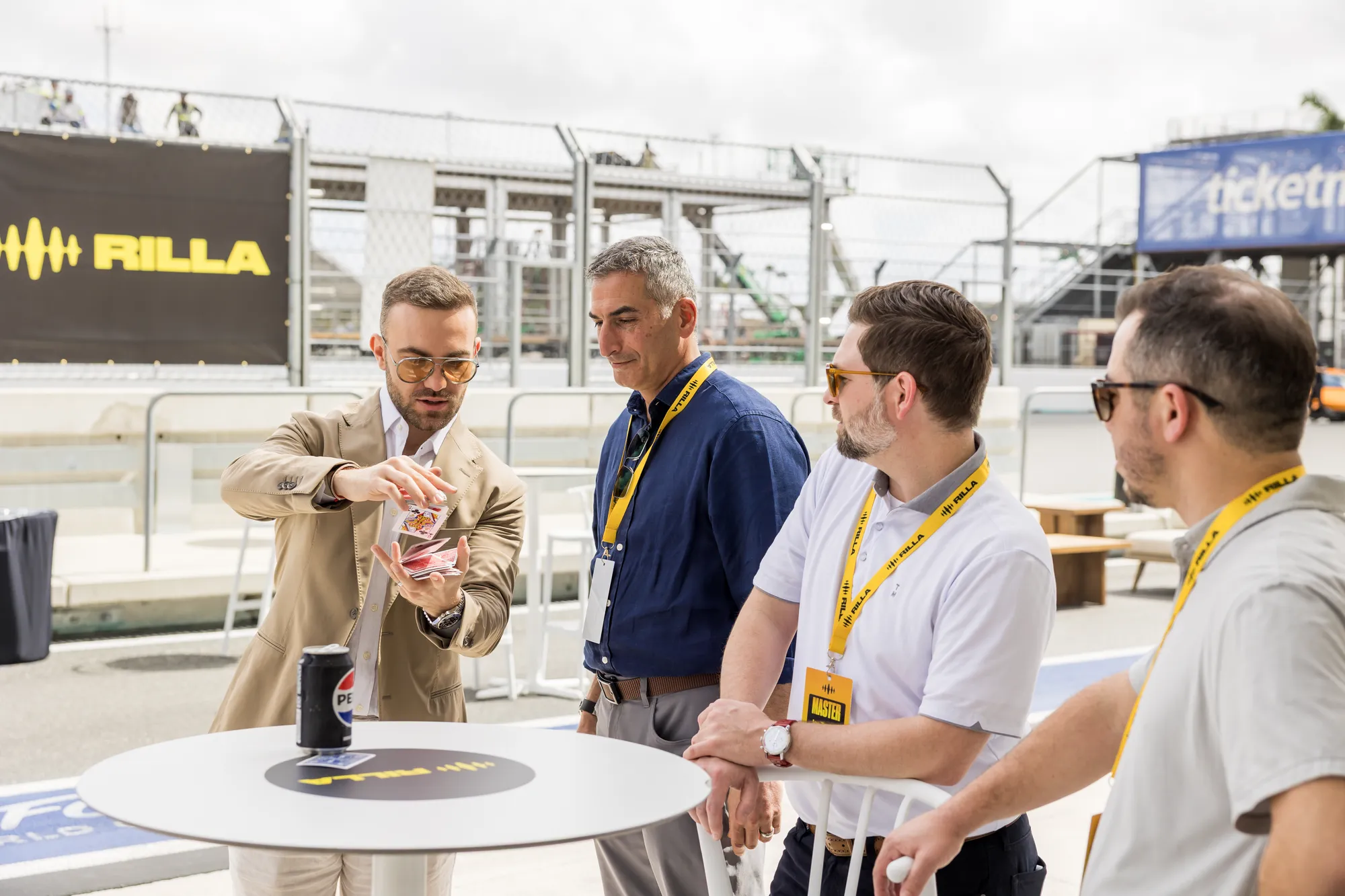 Matteo Cammisa performing card magic trackside at the Miami International Autodrome with the circuit fencing and grandstands behind