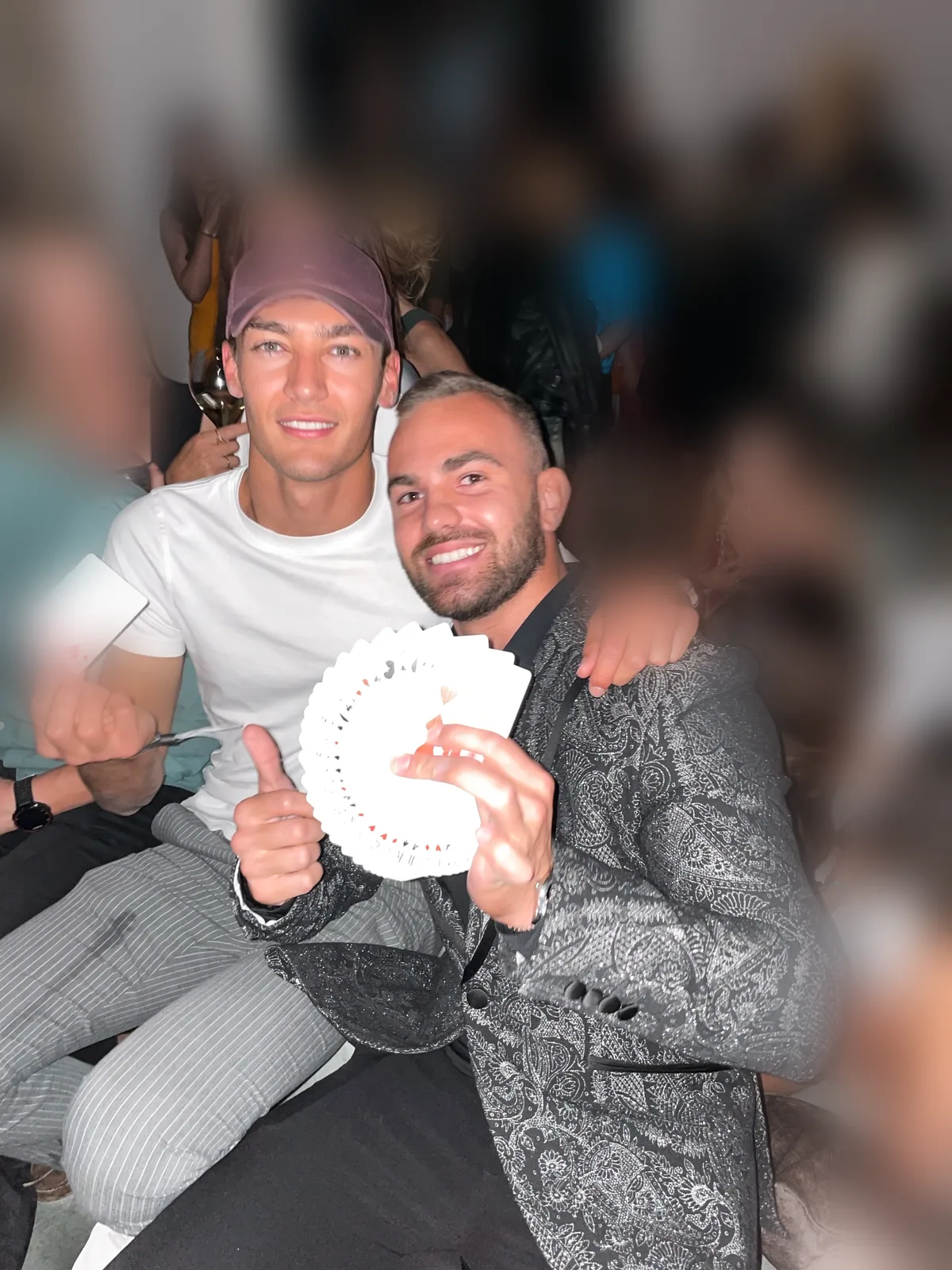 George Russell giving a thumbs up beside magician Matteo Cammisa, who fans a deck of cards with a signed card at its center