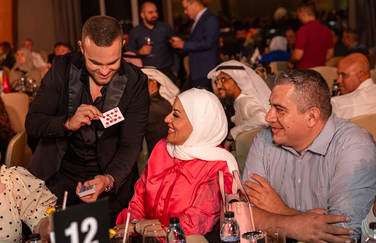 Matteo Cammisa showing a playing card to smiling seated guests during table-hopping close-up magic at the SGS Dental Congress gala in Dubai