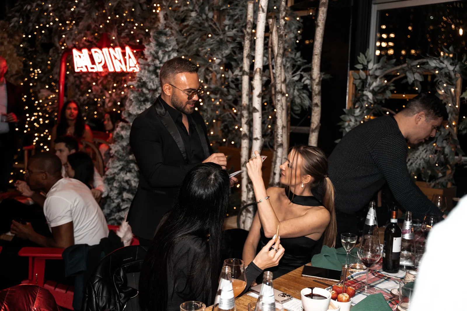 Matteo Cammisa performing card magic beside the ALPINA neon sign at the Eataly rooftop, with the Manhattan skyline beyond