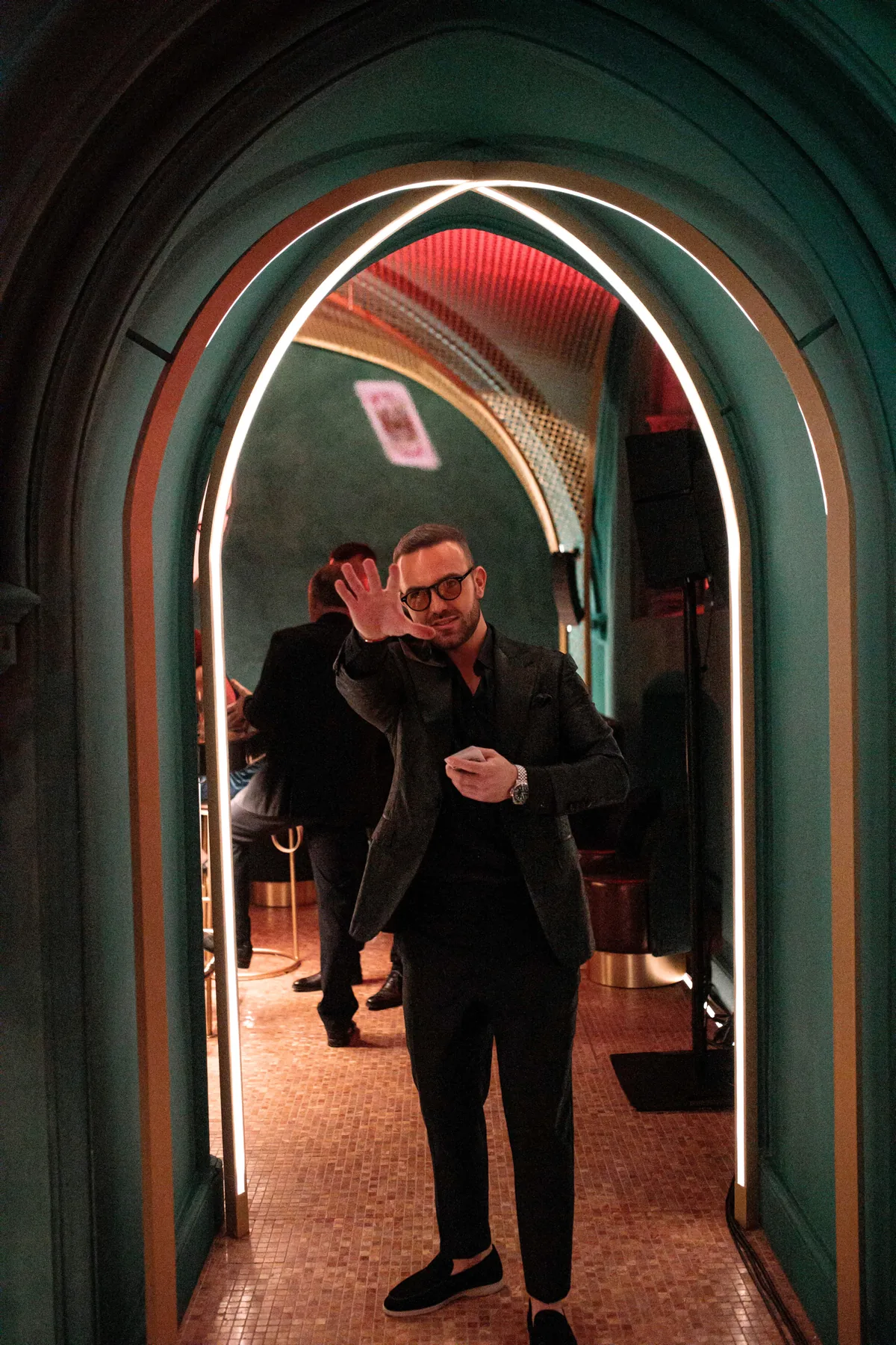 Matteo Cammisa throwing a playing card into the air beneath the illuminated arch of W Budapest's green corridor